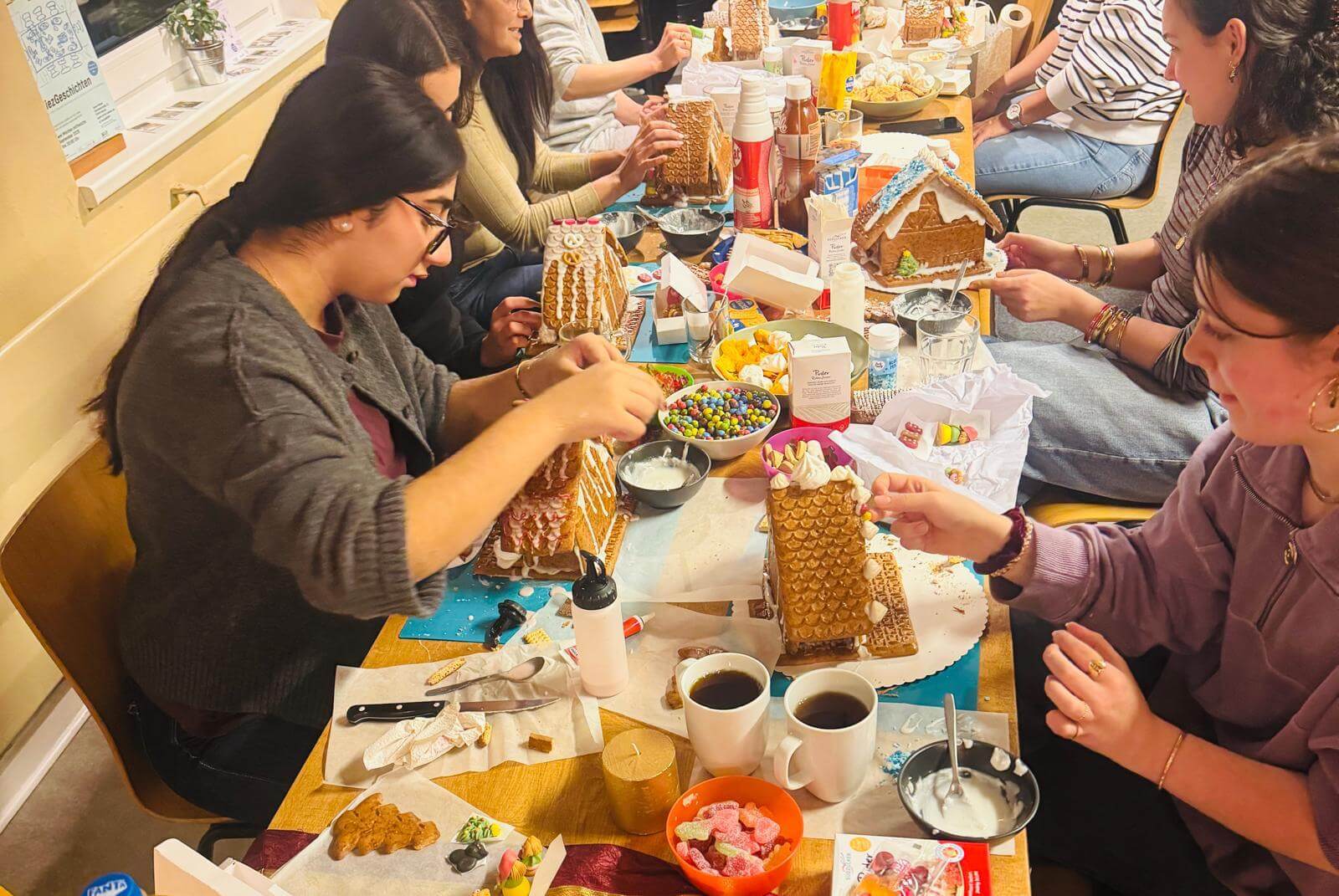 Kadınlar masada oturuyor. Zencefilli kurabiye evleri süslüyorlar.