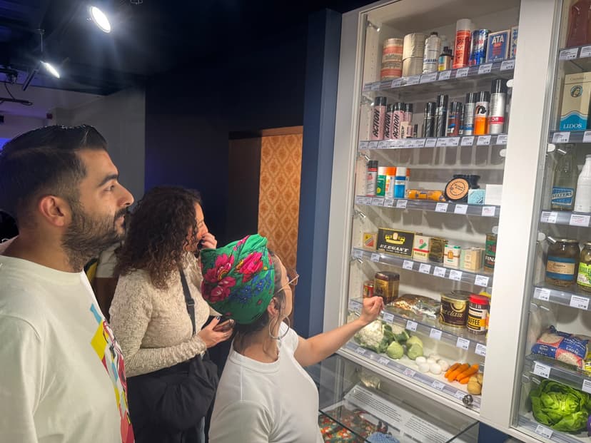 Drei Personen schauen sich eine Vitrine an mit Kosmetikartikeln aus der DDR